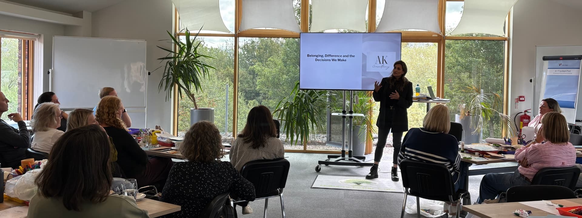 Anira Khokhar standing at the front of a room addressing a workshop of seated attendees, with her presentation on screen behind her