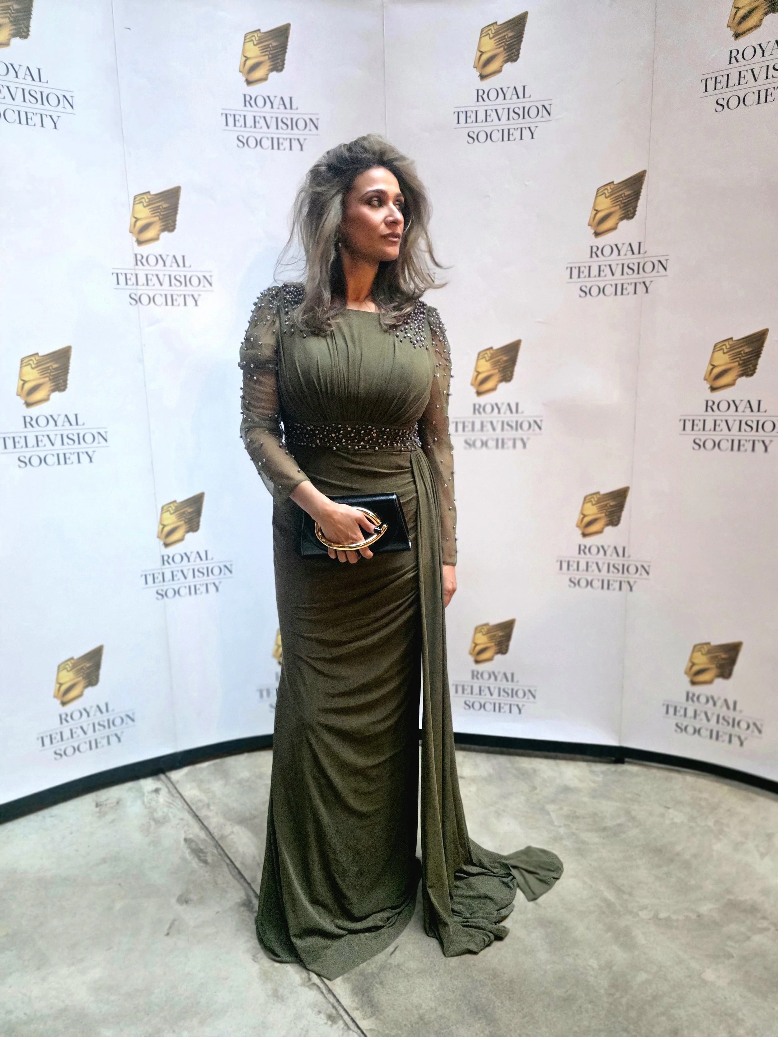 Anira Khokhar in full-length evening dress in front of the Royal Television Society backdrop at the Royal Television Society Awards
