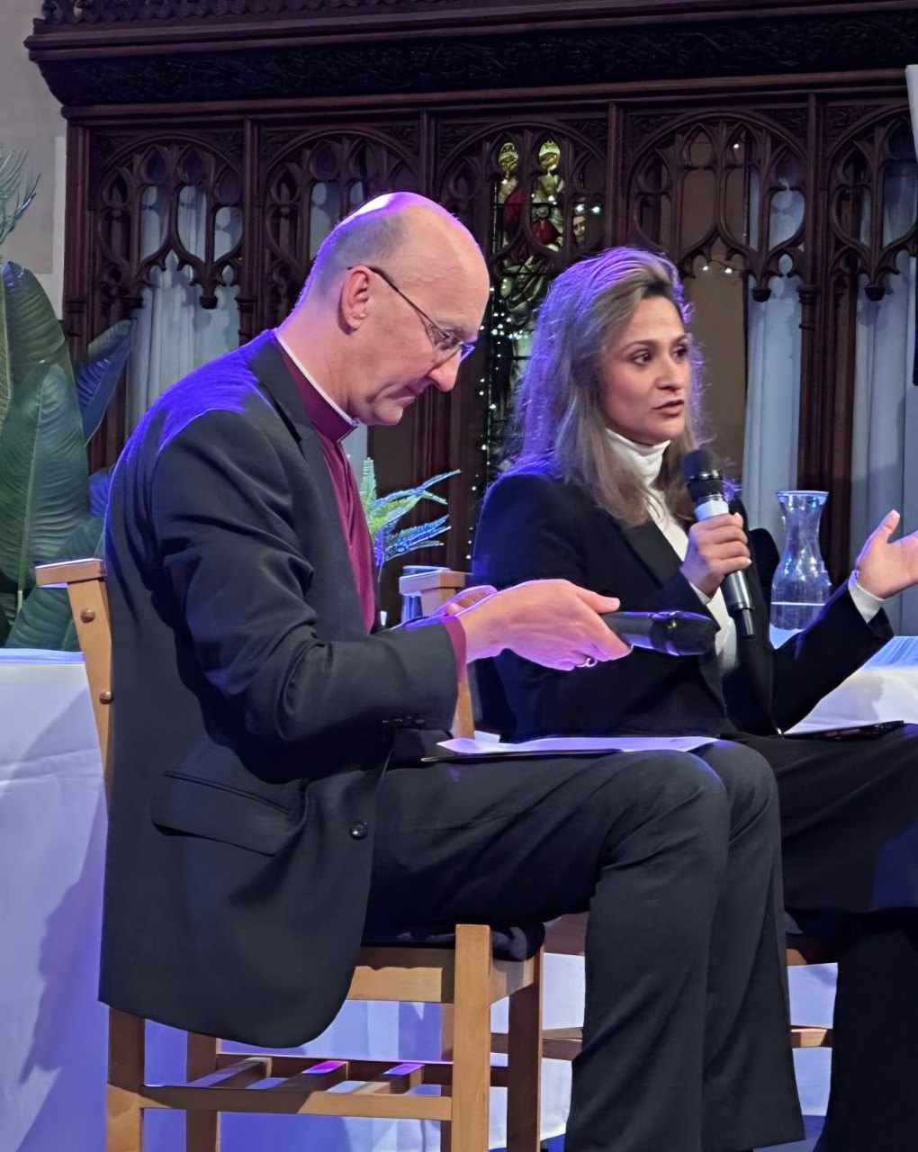 Anira Khokhar speaking on a panel in a church, holding a microphone