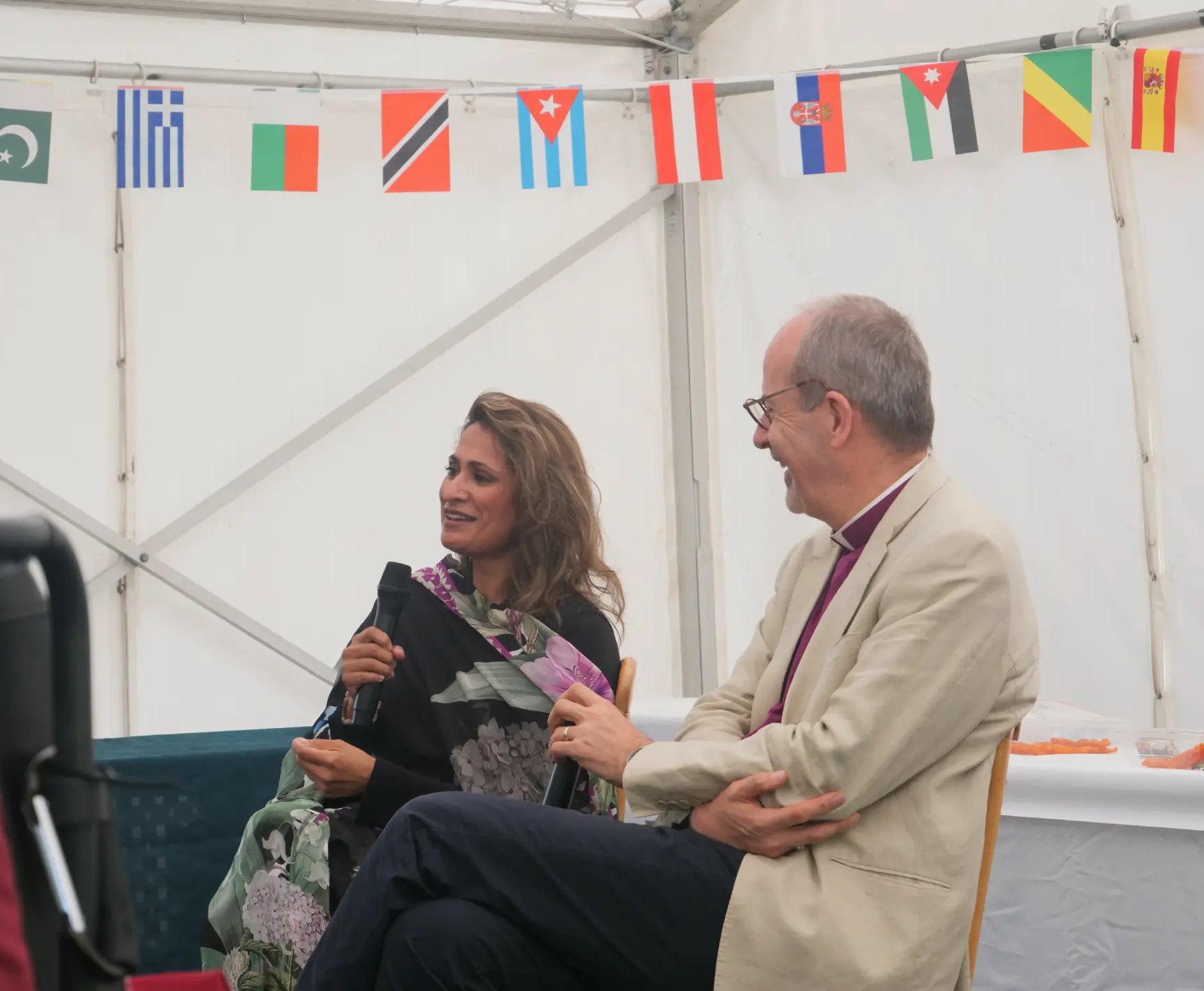 Anira Khokhar in conversation with a member of the clergy at an outdoor event, with international flags strung above